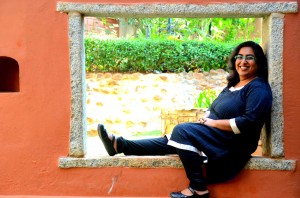 The author in a black and silver salwar kameez, smiling, seated, one leg outstretched, outdoors in Bangalore, India.
